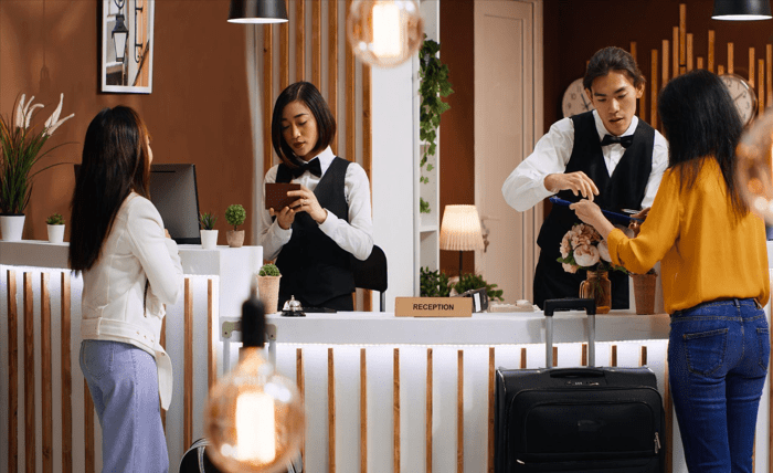 Why Hospitality Industries Should Use Google Ads to Increase Bookings Two hotel staff members assist two tourists at the reception desk.
